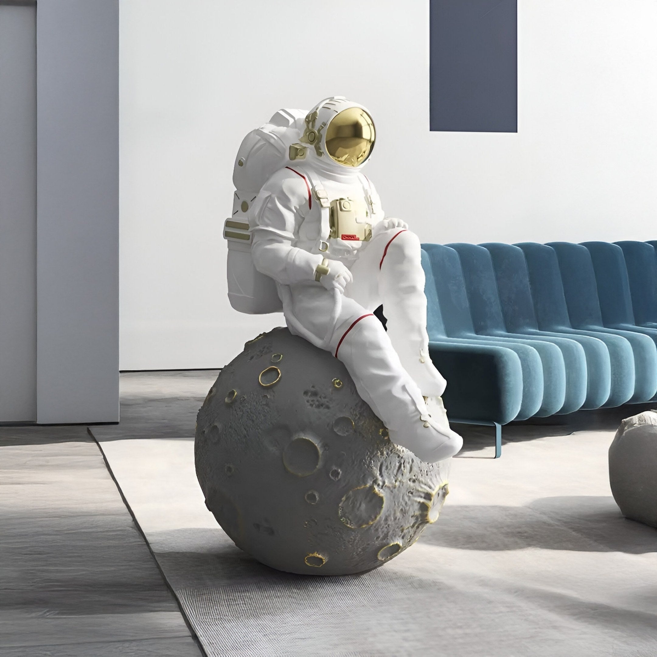 The White Space Astronaut Moon Rest Sculpture by Giant Sculptures enhances a minimalist room. The 100cm astronaut, in a detailed spacesuit and reflective visor, perches on a moon-like sphere. Sunlight highlights the blue couch, emphasizing space exploration in this serene white space.