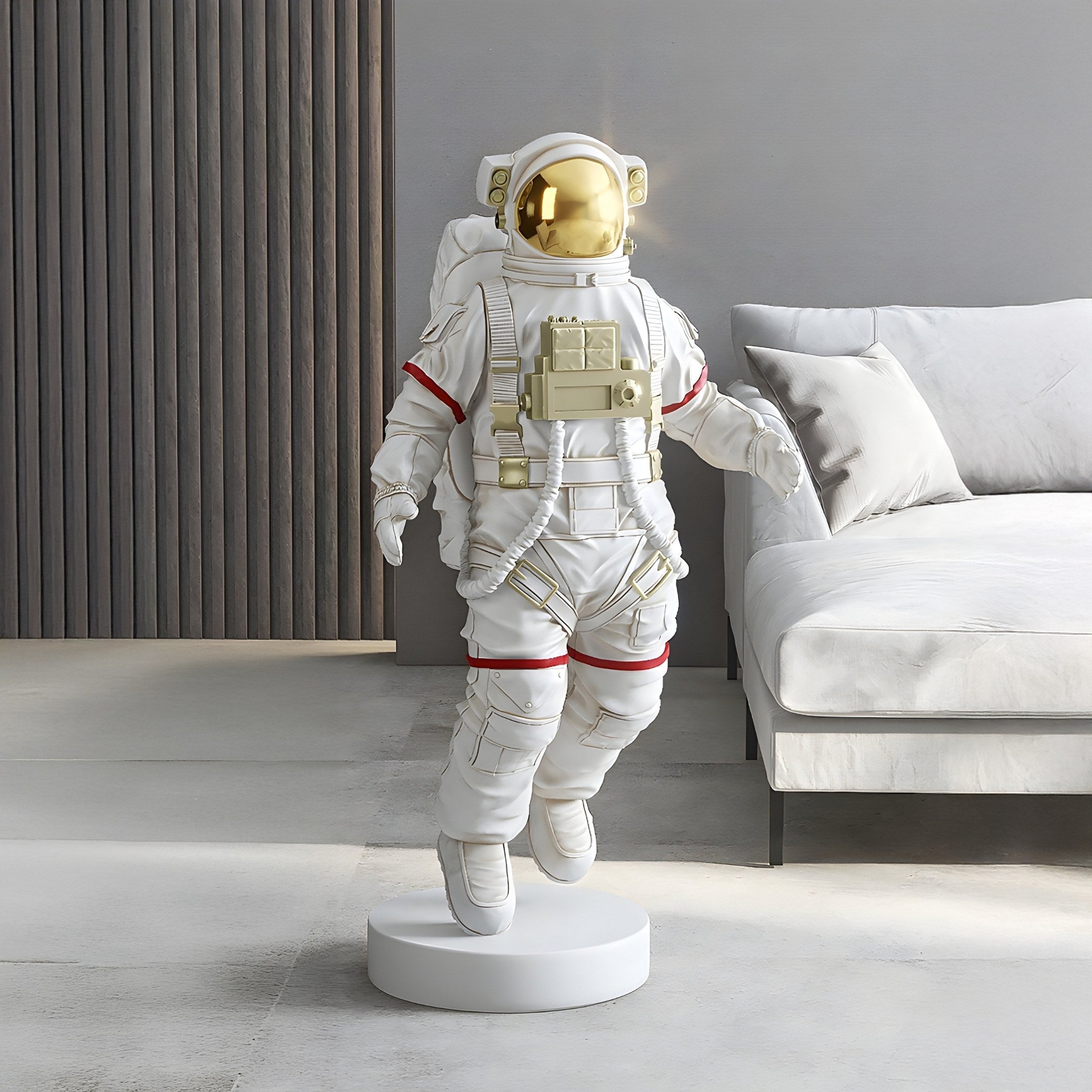 A modern room features the 100cm Cloud White Space Astronaut Voyager Sculpture by Giant Sculptures, showcasing a gold visor atop a circular base. Its placed near a light gray sofa and set against a dark textured panel, balancing contemporary and space themes.