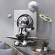 A Silver Balloon Astronaut figure with a reflective helmet sits on a floating platform, holding a moon-shaped balloon. The 3D Portal Wall Art by Giant Sculptures features planets and rings in its cosmic-themed background with an astronaut figurine resting nearby.