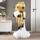 Celestial Gold Astronaut Glow Lift-Off Sculpture by Giant Sculptures, 110cm resin figure in metallic gold with black gloves and boots, holding a glowing orb, rising from a white cloud base, shown in a modern living room.