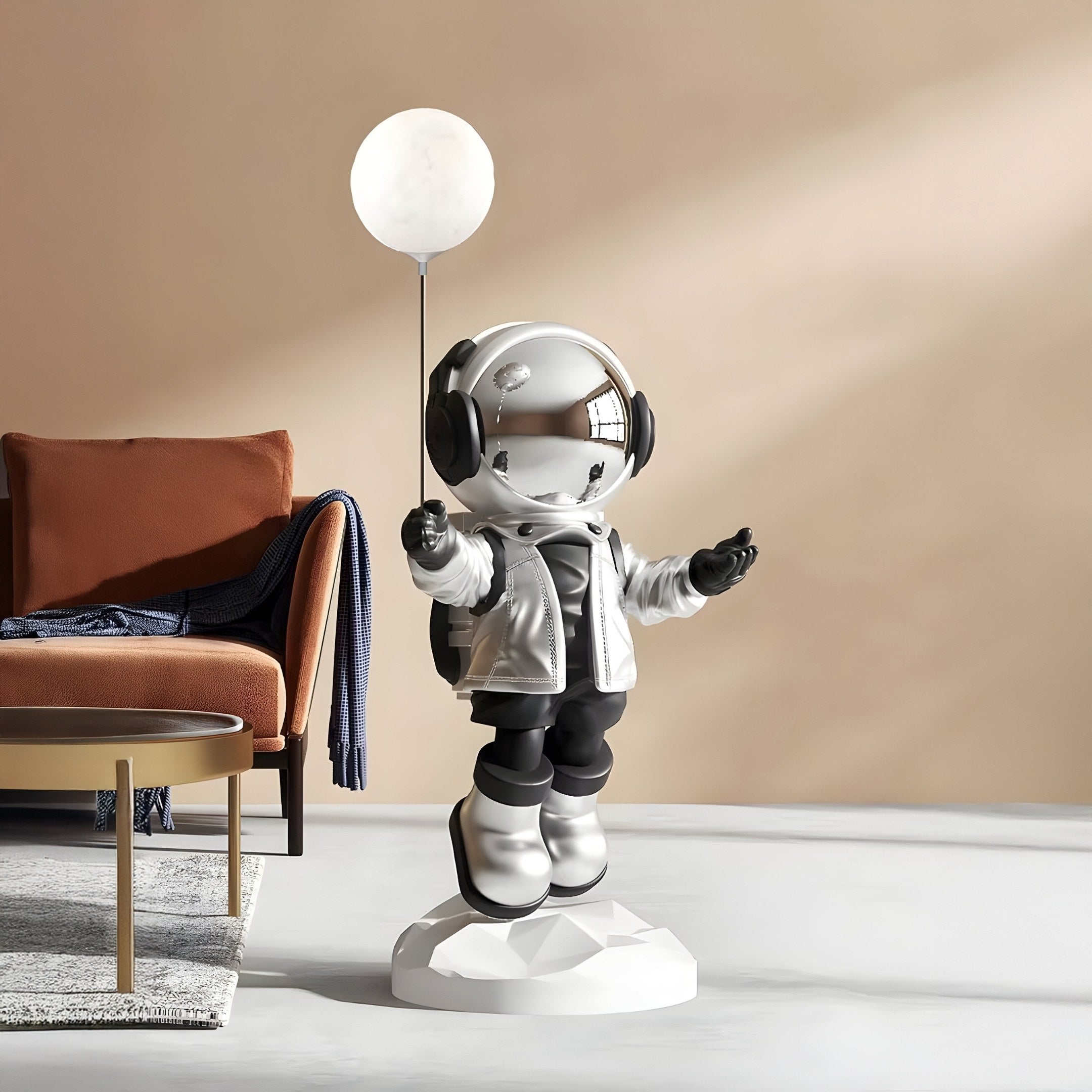 The Lunar Silver Astronaut Glow Balloon Sculpture - 110cm by Giant Sculptures features a metallic astronaut holding a glowing balloon on a white base, with black gloves and boots, perfectly complementing an orange couch and blue blanket in this modern living room.