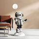 The Lunar Silver Astronaut Glow Balloon Sculpture - 110cm by Giant Sculptures features a metallic astronaut holding a glowing balloon on a white base, with black gloves and boots, perfectly complementing an orange couch and blue blanket in this modern living room.