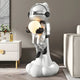 Lunar Silver Astronaut Glow Lift-Off Sculpture by Giant Sculptures, 110cm resin figure in silver with black gloves and boots, holding a glowing orb atop a cloud base, shown in a modern living room.