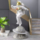 White Space Astronaut Ringed Moon Strider Sculpture by Giant Sculptures, 118cm resin figure in white suit with gold visor mid-stride above a cratered ringed moon base, displayed beside a staircase.