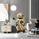 The Celestial Gold Astronaut Ranger Glow Balloon Sculpture (120cm) by Giant Sculptures adds an enchanting cosmic style to a modern living room, floating on a white platform among a gray sofa, abstract art, and decorative plants.