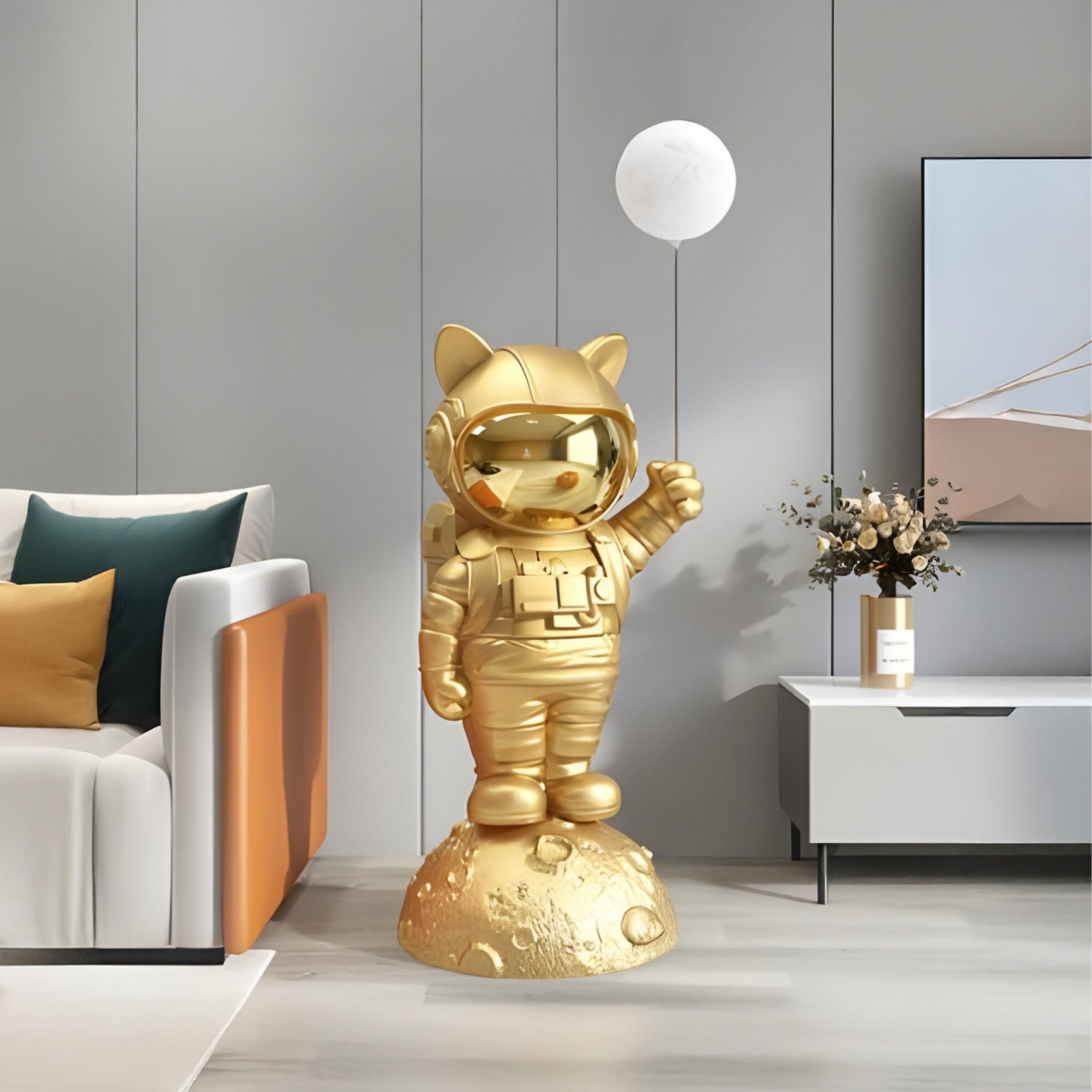 The Gilded Gold Astronaut Kitty Glow Balloon Sculpture by Giant Sculptures, standing 120cm tall with cat ears and a white balloon, is a focal point of a space-themed interior featuring elements like a modern living room sofa, wall art, and a table adorned with a flower vase.