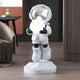 The Lunar Silver Astronaut Glow Hover Sculpture - 80cm by Giant Sculptures features a small silver astronaut on a geometric base, holding a glowing orb. With its reflective visor and sleek white spacesuit, it adds futuristic charm to any modern room beside the bed or side table.