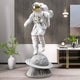 White Space Astronaut Ringed Moon Explorer Sculpture by Giant Sculptures, 125cm resin figure in white with gold visor, mid-step above a cratered grey moon base with ring, shown in a modern living space.