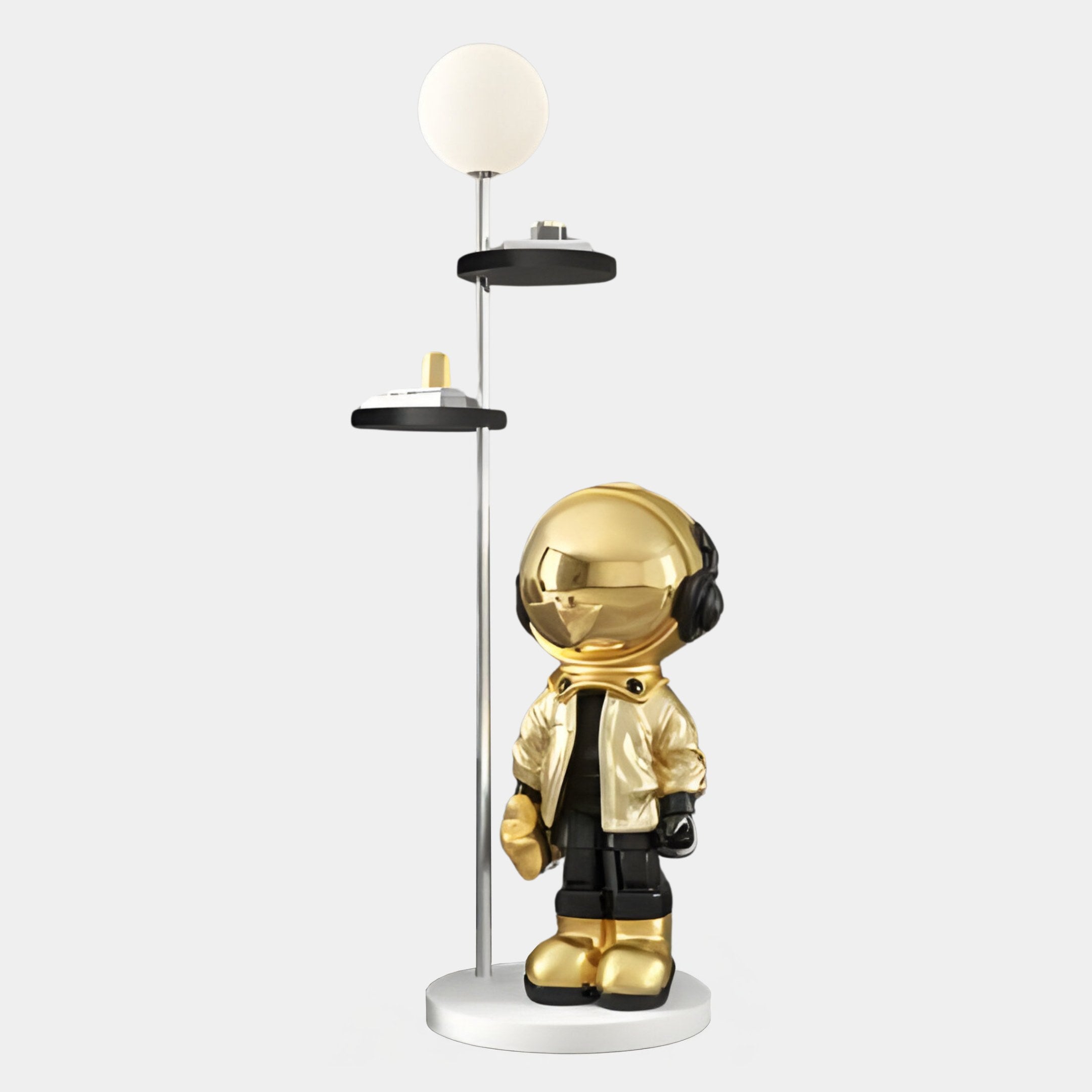 The Gold Astronaut Beats Floor Lamp With Shelves by Giant Sculptures is a modern décor piece featuring a metallic robot figure with a jacket and headphones. It stands on a circular base, includes two shelves, and has a round light fixture atop the 135cm vertical pole, offering style and functionality.