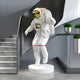 The Giant Sculptures White Space Astronaut Explorer Sculpture stands 150cm tall, featuring a realistic design with a golden visor and intricate spacesuit details, all atop a circular platform in an interior accented with gray and metallic elements.