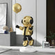 The Celestial Gold Astronaut Moon Balloon Sculpture from Giant Sculptures features a gold and black astronaut with headphones, standing on a white base, holding a moon balloon. This 160cm sculpture complements modern decor with plants, books, and art for a sleek futuristic vibe.