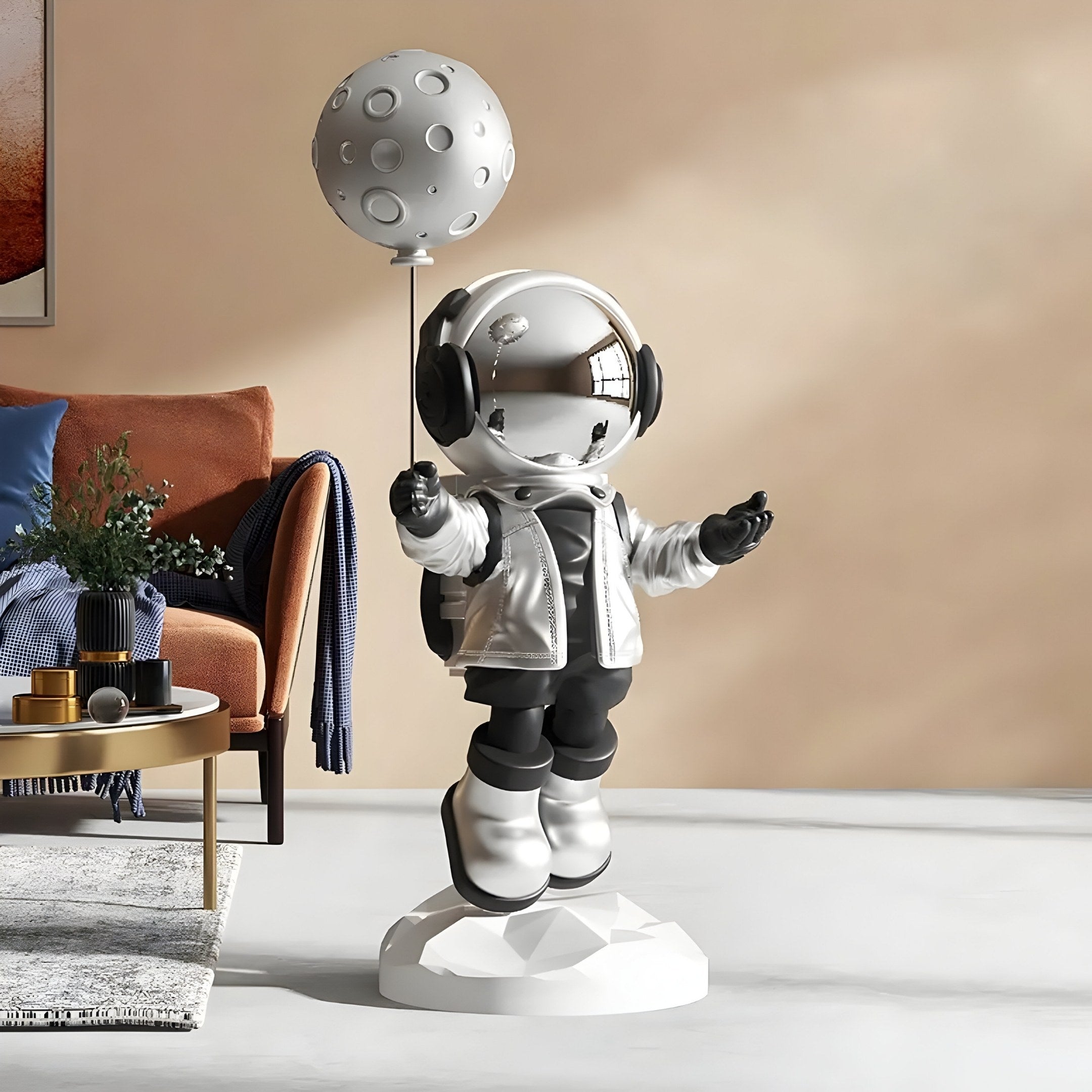 The Lunar Silver Astronaut Moon Balloon Sculpture by Giant Sculptures, featuring a glossy figurine with a reflective helmet holding a moon-shaped balloon, stands on a geometric white base in the modern living room beside a brown couch and decor, enhancing the futuristic ambiance.