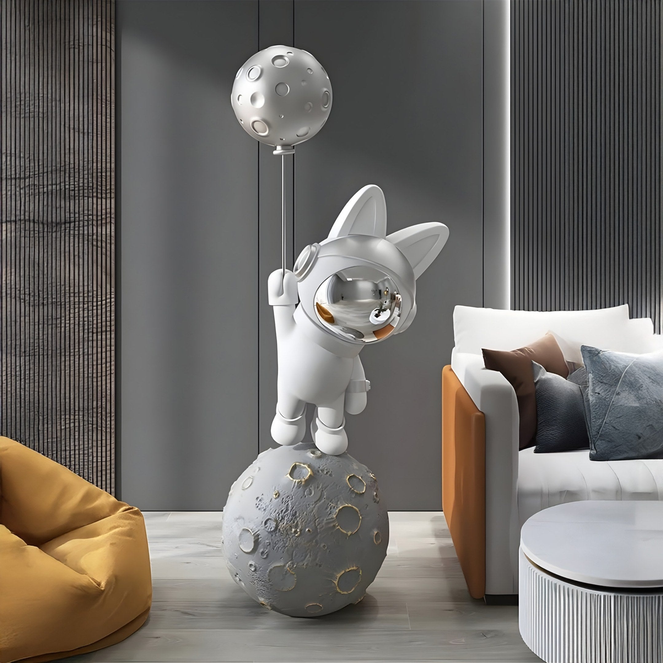 The Giant Sculptures Cosmic Chrome Astronaut Bunny Moonwalk Balloon Sculpture (180cm) features a cute bunny with cat-like ears balancing on a moon-like sphere, displayed in a modern living room with a gray wall, white sofa adorned with pillows, and a mustard bean bag.