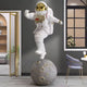 The White Space Astronaut Moon Strider Sculpture - 210cm by Giant Sculptures features a modern astronaut with a gold visor balancing on a moon sphere—an eye-catching piece to elevate stylish contemporary interiors.