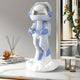 The Cosmic Sky Blue Astronaut Lift-Off Mini Figure (30cm) by Giant Sculptures features a shiny helmet and blue accents, standing on a white cloud atop a marble table—perfect for modern interiors with candles, a diffuser, and framed art.
