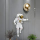 The White 3D Cosmic Lift Balloon Astronaut Wall Art by Giant Sculptures features an astronaut in a white suit with red accents and a gold balloon. Perfect as wall art against textured gray, complemented by plants below, it elevates home decor. Size: 40cm.