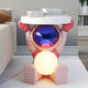 The Giant Sculptures Stellar Pink Astronaut Glow Side Table Figure (50cm) features a reflective-helmet astronaut holding a round white tabletop and glowing sphere, making it a stylish ambient light side table for modern living rooms.