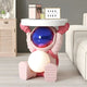 The Stellar Pink Astronaut Glow Side Table Figure (50cm) by Giant Sculptures supports a round white tabletop with a framed Home Sweet Home sign, gift box, and candle. The modern room features ambient light and astronaut-themed decor accents.