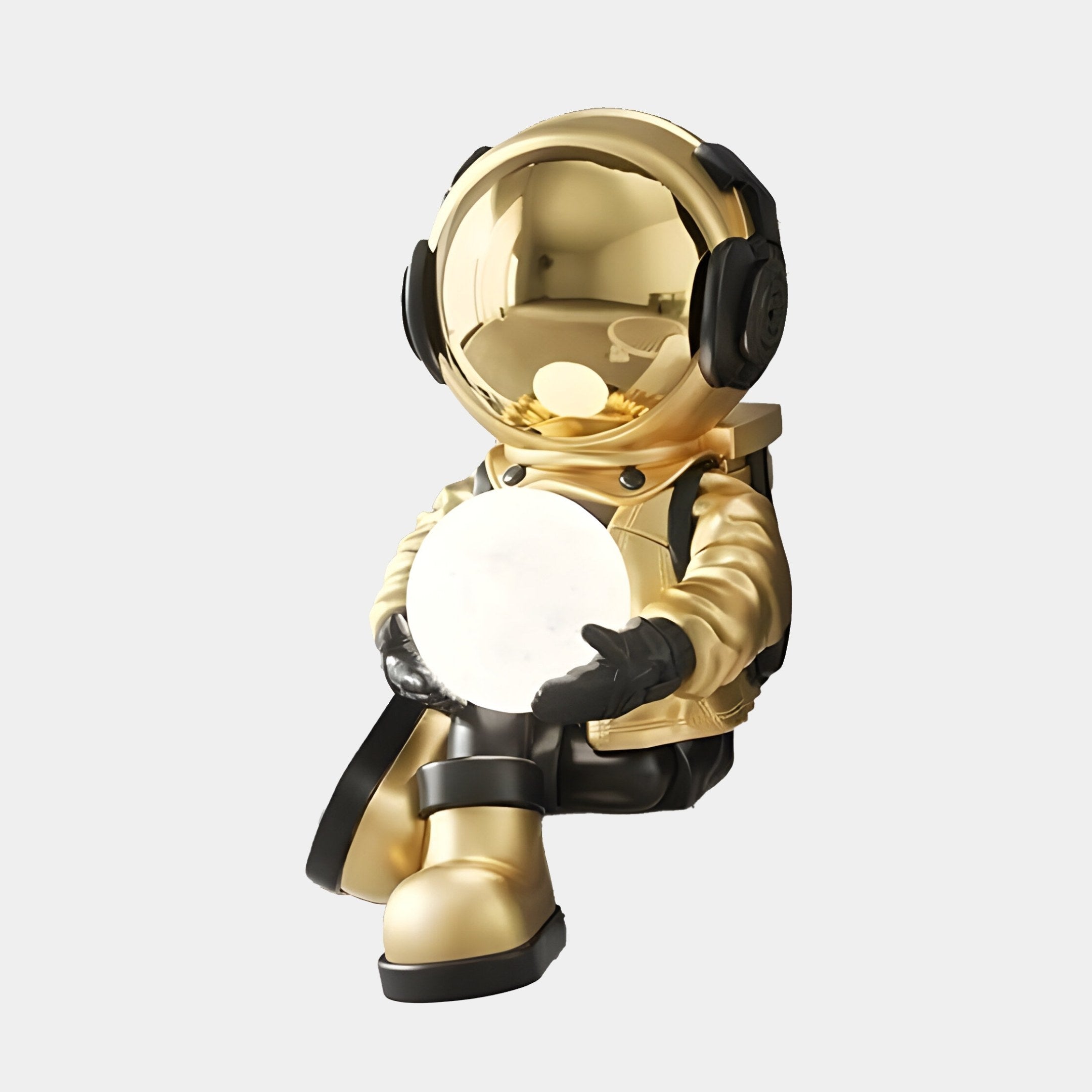 The Celestial Gold Astronaut Glow Seated I Sculpture by Giant Sculptures is a 53cm decorative gold lamp with a cross-legged astronaut in celestial style. Its reflective helmet and glowing sphere add intrigue to any setting, while adjustable lighting colors enhance its charm against the white background.