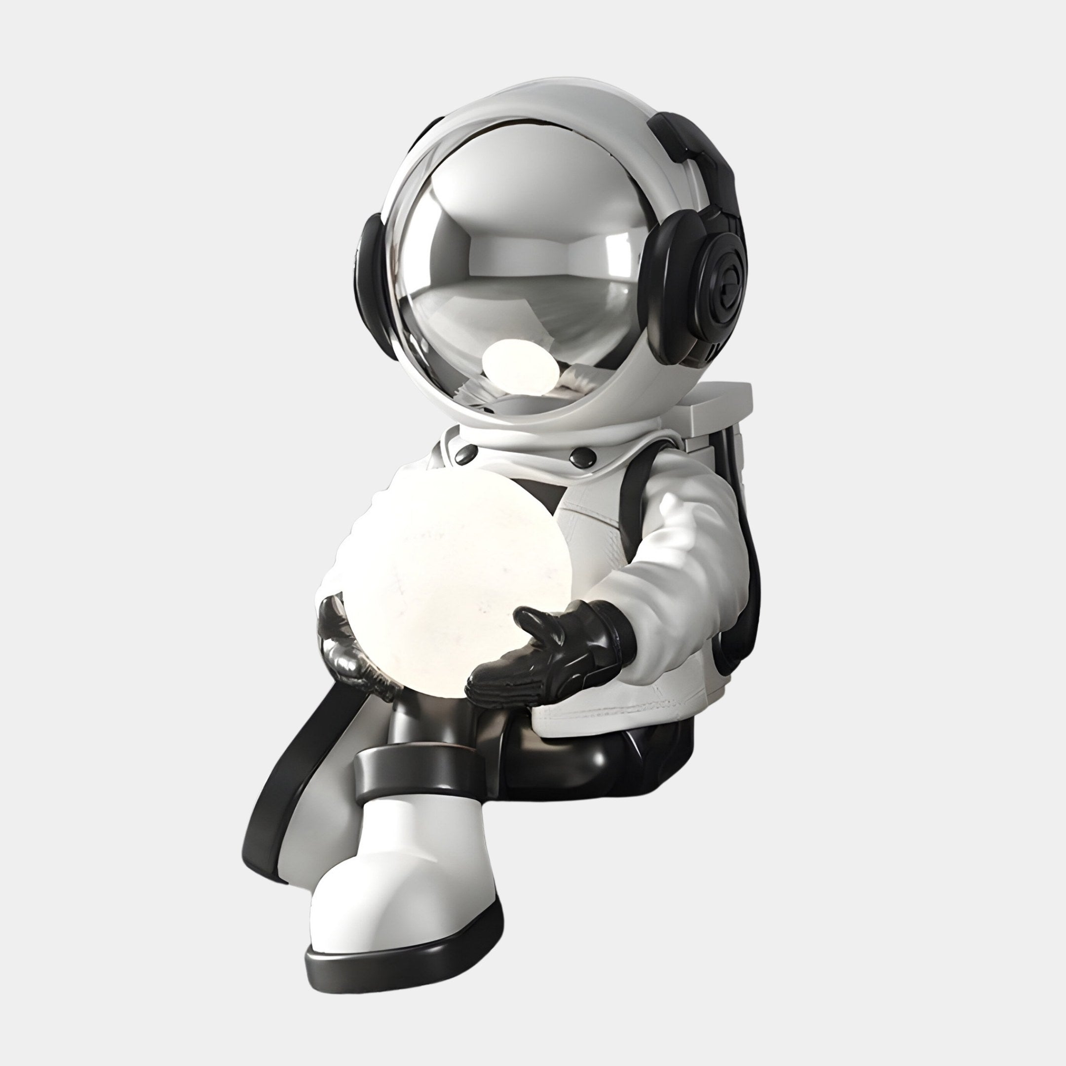 The Lunar Silver Astronaut Glow Seated I Sculpture by Giant Sculptures features a shiny, reflective helmet and holds a glowing orb. With adjustable lighting colors, USB charging, and sleek white with black accents, this 53cm piece enhances any space against its plain white backdrop.