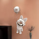The Giant Sculptures Chrome Astronaut Bunny Balloon 3D Wall Art (70cm) features a white bunny floating with a moon-shaped balloon, adding whimsical charm above a black cabinet beside a vase of dried flowers.