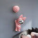 The Pink Astronaut Bunny Balloon 3D Wall Art (70cm) by Giant Sculptures features a pink bunny with a shiny silver faceplate hanging from a balloon shaped like a pink moon, displayed above a modern couch with black and pink cushions.