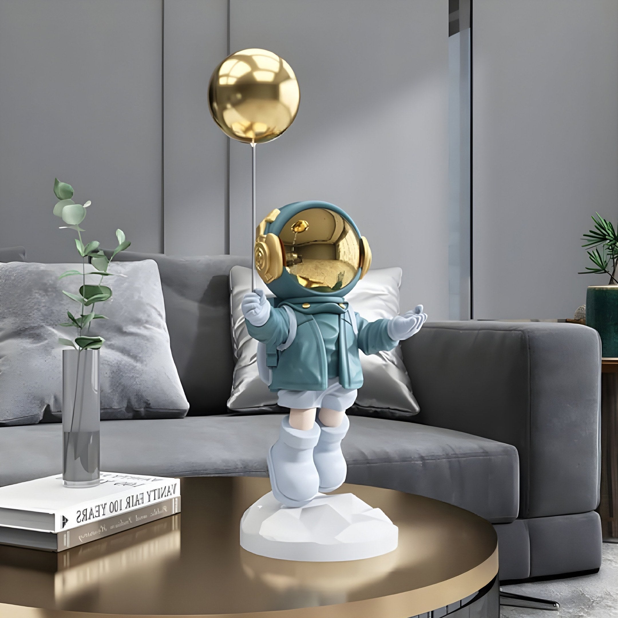 The Galactic Blue Astronaut Balloon Sculpture by Giant Sculptures stands at 55cm, featuring a blue suit and gold balloon on a geometric base. It elegantly complements a modern living room table, gray couch, plant, and books.