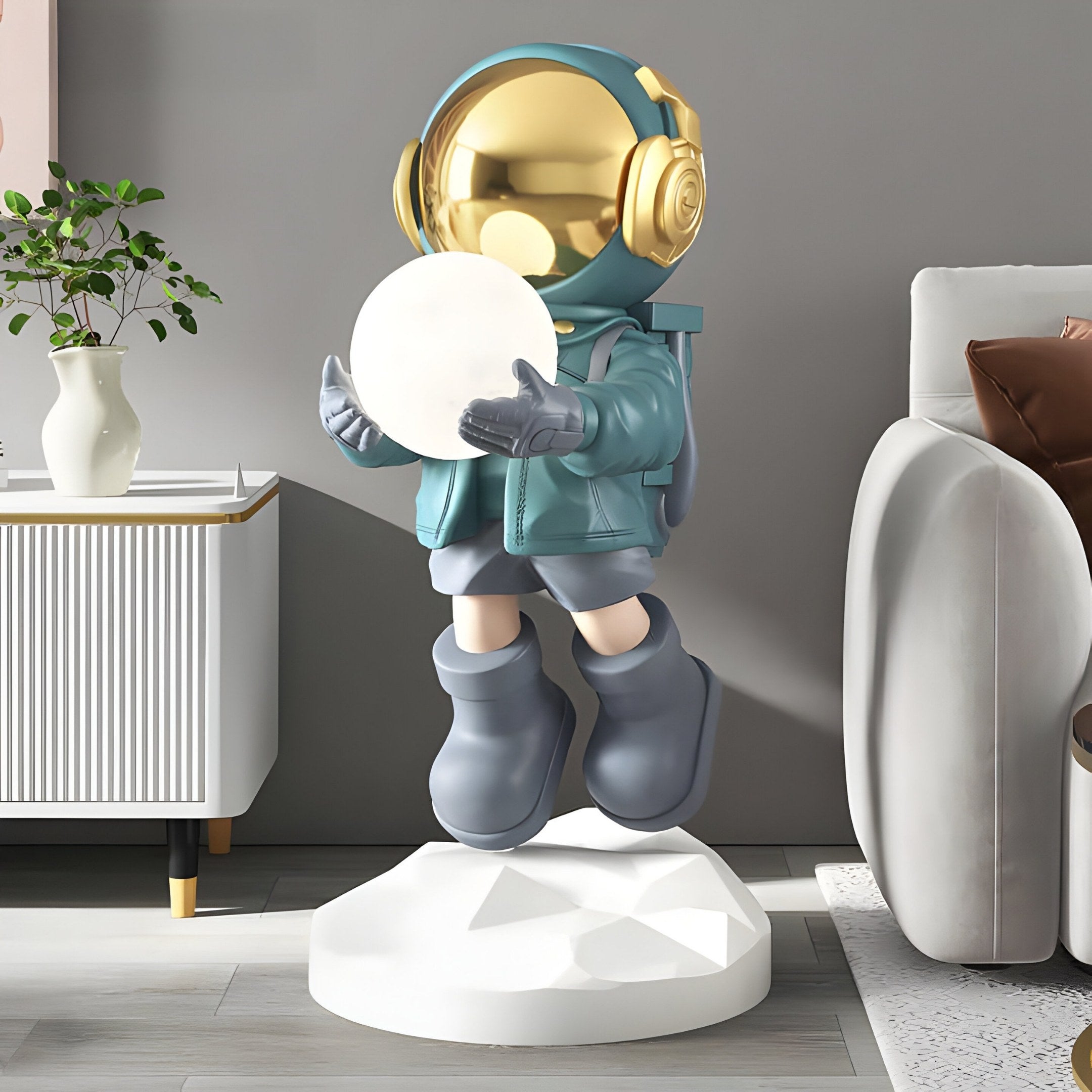 The Giant Sculptures Galactic Blue Astronaut Glow Hover Sculpture stands 60cm tall with a reflective gold helmet and headphones on a geometric white base. It holds a glowing orb, adds flair to any modern living room, and features USB charging for added functionality.