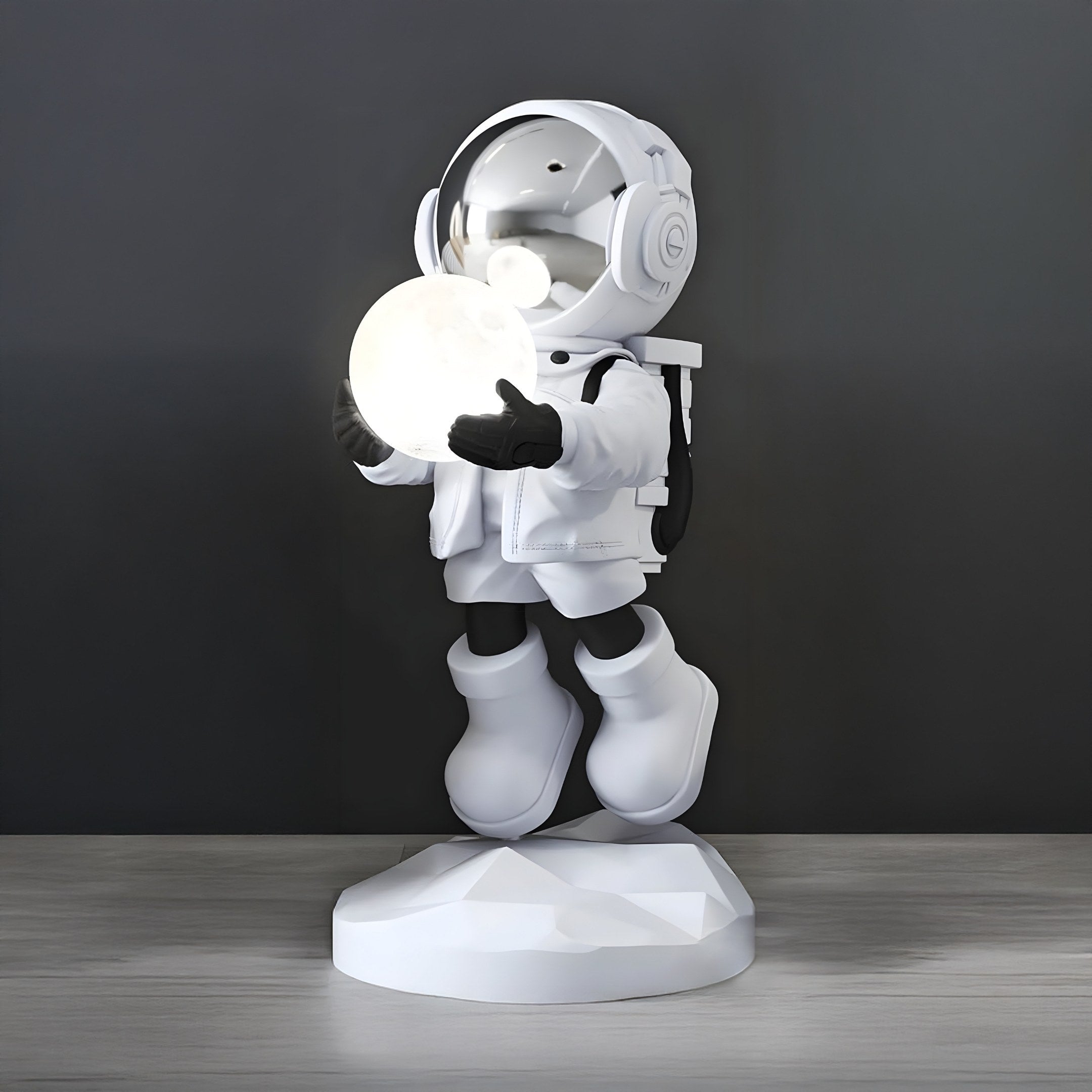 The Nova White Astronaut Glow Hover Sculpture by Giant Sculptures is a 60cm cartoon-style figurine that serves as a lamp with a glowing sphere on its geometric base. Featuring a reflective helmet and detailed suit, it offers adjustable lighting colors, contrasting the white figure against a gray background.