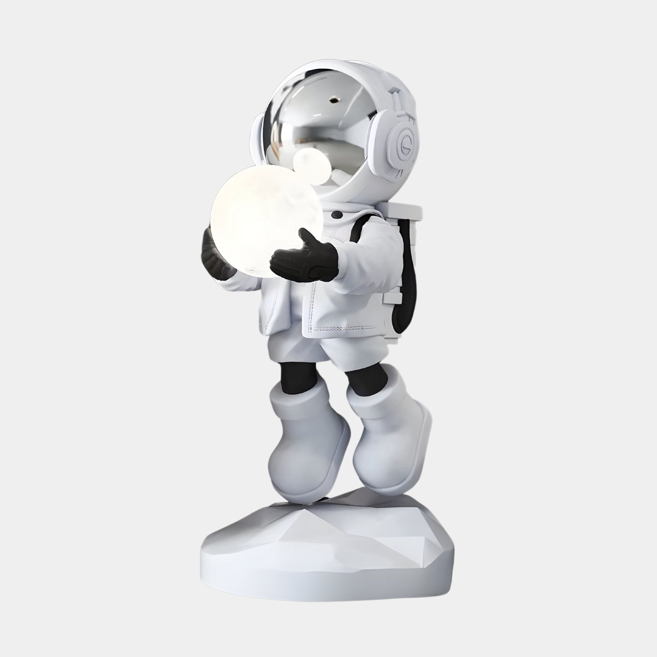 The Nova White Astronaut Glow Hover Sculpture by Giant Sculptures features a stylized astronaut in a reflective white suit with metallic visor, black gloves, and boots. Standing on a rock-like base while holding a glowing orb, it adds modern décor to any space against a plain gray background.