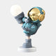 The Giant Sculptures Galactic Blue Astronaut Glow Kick Sculpture (70cm) showcases an astronaut in a gold-visored suit on one leg, orb in hand, standing on a round base with large headphones and set against a light gray background. It features adjustable lighting colors for customizable ambiance.