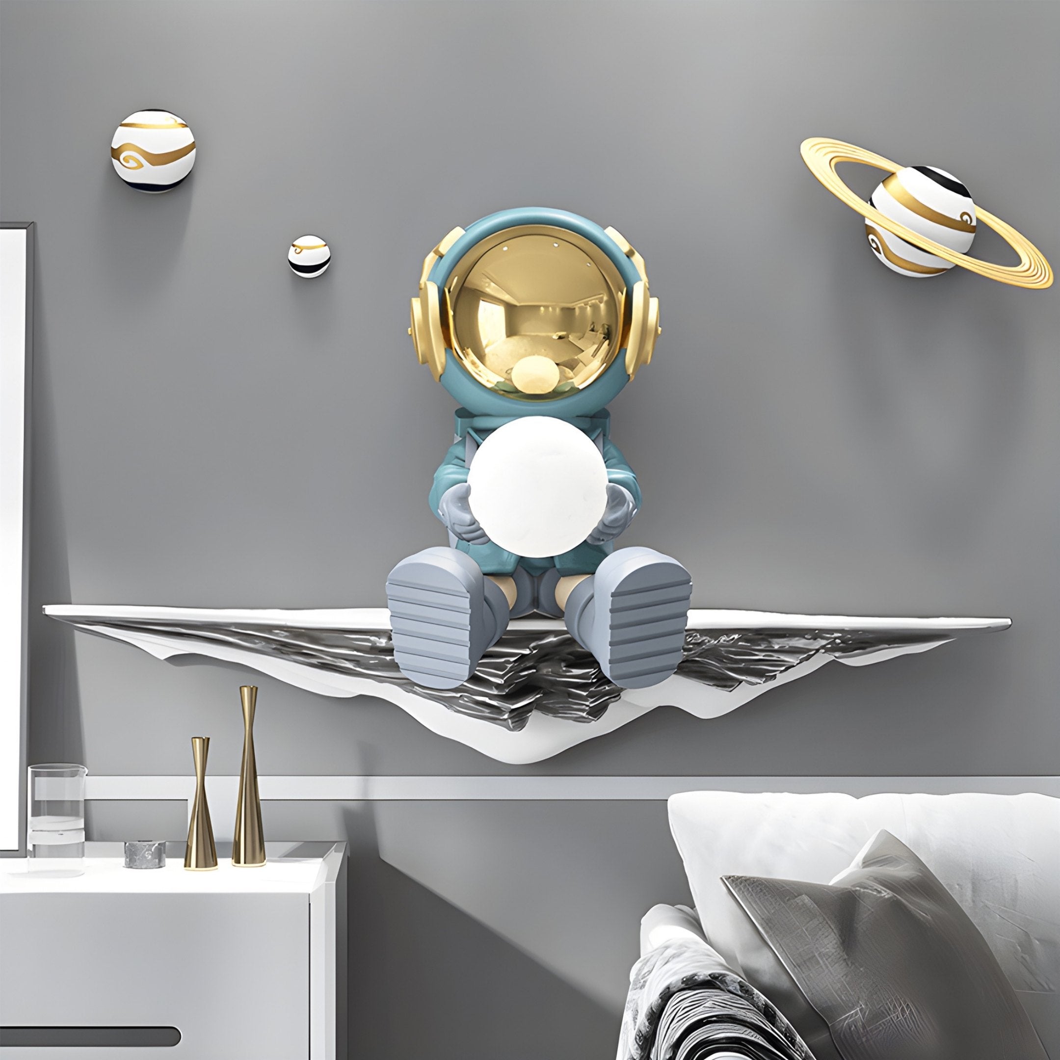 Adorn your wall with Giant Sculptures Blue 3D Dreamer Glow Astronaut Wall Art, showcasing a gold-helmeted astronaut holding a white sphere on a metallic wave shelf against a gray, space-themed background. Complement the look with an elegant white cabinet and sofa ensemble below.