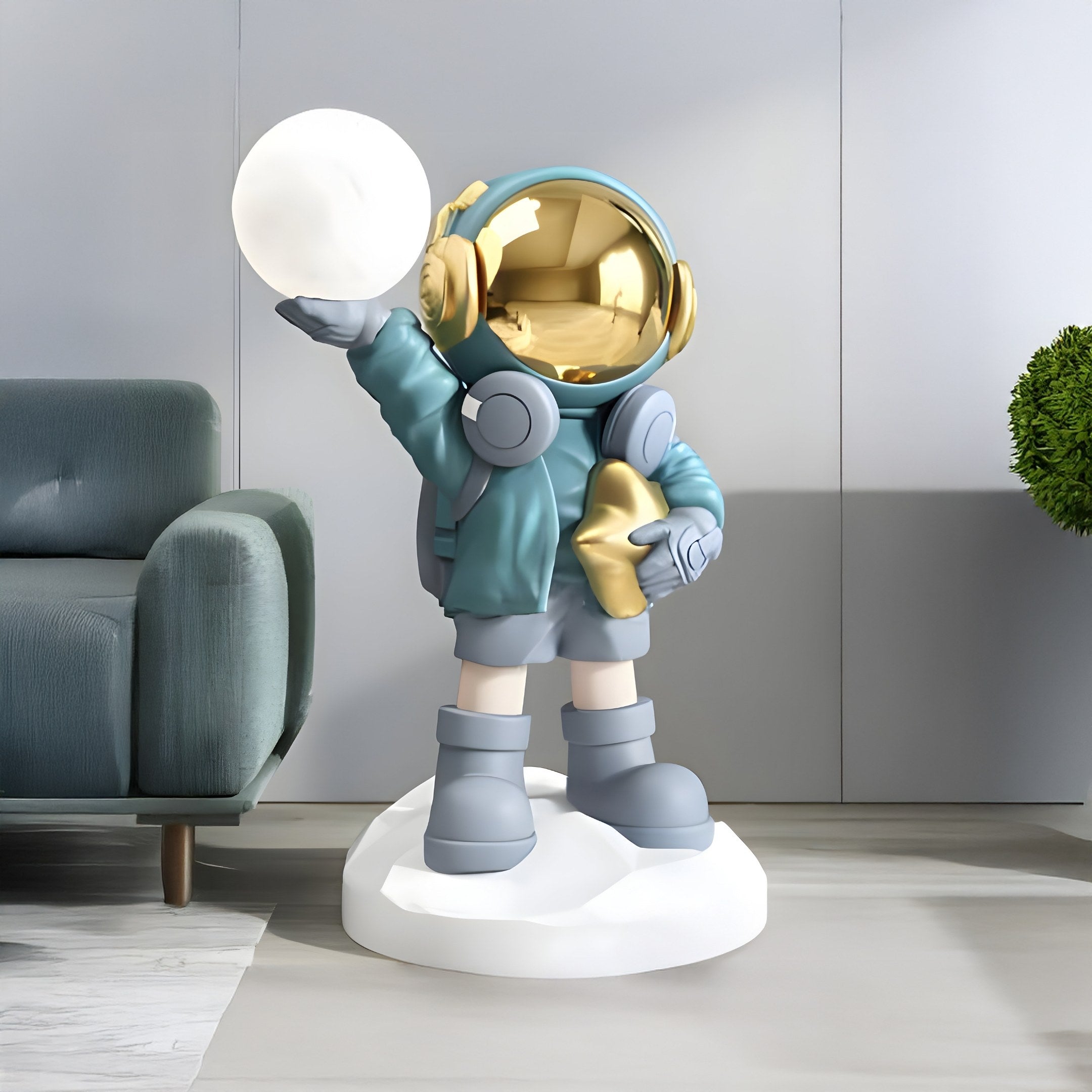 A 75cm Galactic Blue Astronaut from Giant Sculptures, on a white base cradling a Glow Orb Sculpture, features a reflective helmet, teal suit, gray boots, and holds a gold star. A gray sofa and green potted plant complete the space-themed décor.