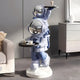 The Cosmic Sky Astronaut Duo Server Sculpture (78cm) by Giant Sculptures features blue and white astronauts with mirrored helmets holding black trays, ideal for displaying drinks or desserts in modern interiors beside sofas or cabinets.