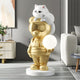 The Gold Astronaut CosmoPals Glow Bear Sculpture by Giant Sculptures, featuring aviator sunglasses, clutches a glowing orb with a white cat perched on its head. This whimsical piece adds futuristic flair to a modern living room with abstract wall art and contemporary furnishings.