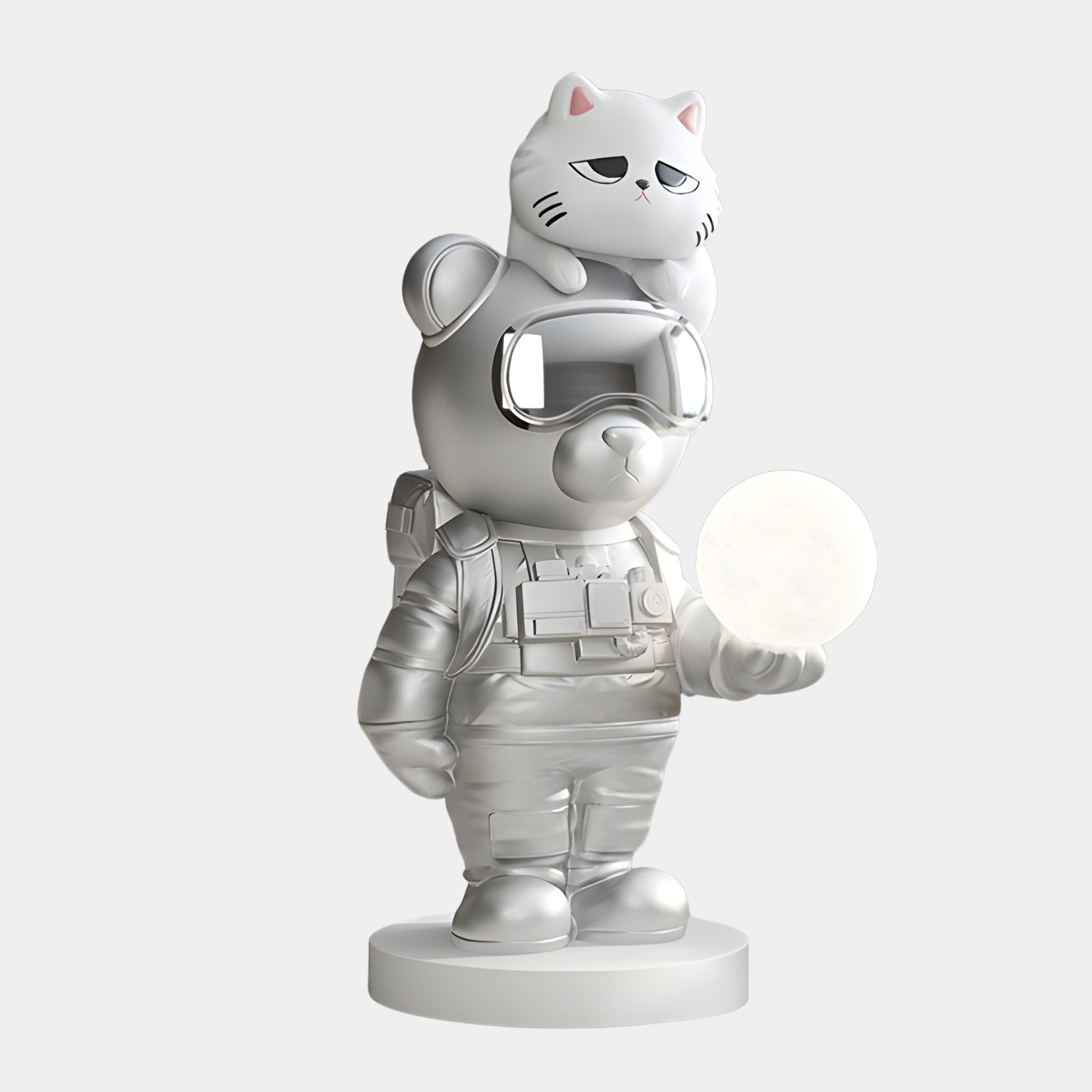 The Chrome Astronaut CosmoPals Glow Bear Sculpture by Giant Sculptures showcases an 80cm silver toy bear in a spacesuit, with large goggles and a cat on its head, holding a white circle on a round base in minimalistic and futuristic style.