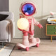 The Giant Sculptures Stellar Pink Skater Astronaut Glow Sculpture (80cm) features a shiny visor and skateboard, holding a glowing orb to brighten modern interiors beside your couch or playful green-and-yellow cabinet.