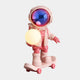 The Stellar Pink Skater Astronaut Glow Sculpture - 80cm by Giant Sculptures features a reflective-helmet astronaut on a skateboard holding a glowing yellow sphere—an eye-catching décor piece for modern interiors.