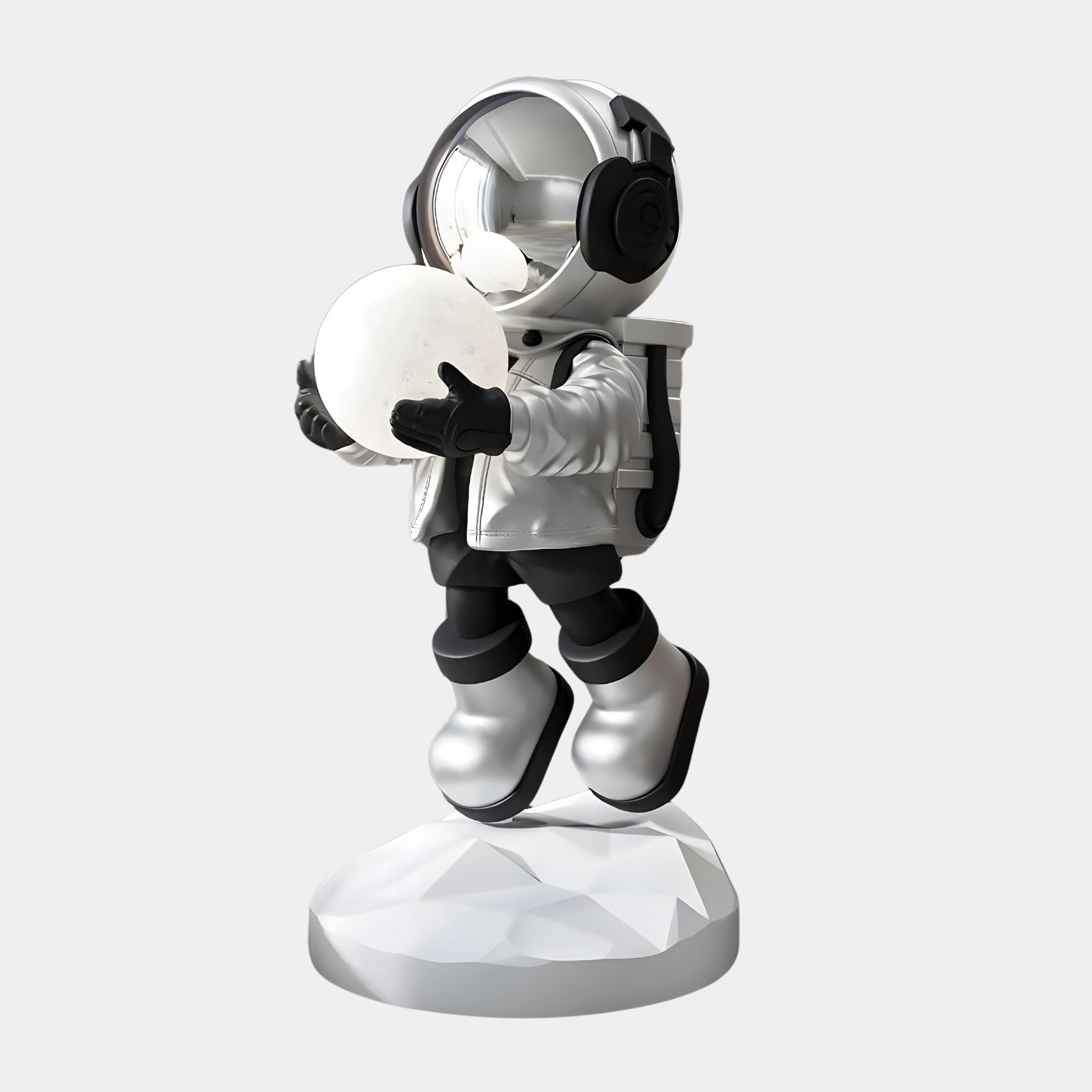 The Lunar Silver Astronaut Glow Hover Sculpture by Giant Sculptures, standing 80cm tall, features a stylized astronaut in a shining suit with a reflective visor on a round platform, holding a white sphere. It has black gloves, boots, and backpack, exuding a sleek and futuristic vibe under adjustable lighting.