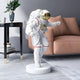 The White Space Astronaut Explorer Sculpture by Giant Sculptures, standing at 85cm with a gold visor, adds a cosmic flair to a modern living room with a beige couch and black side table adorned with green leaves.