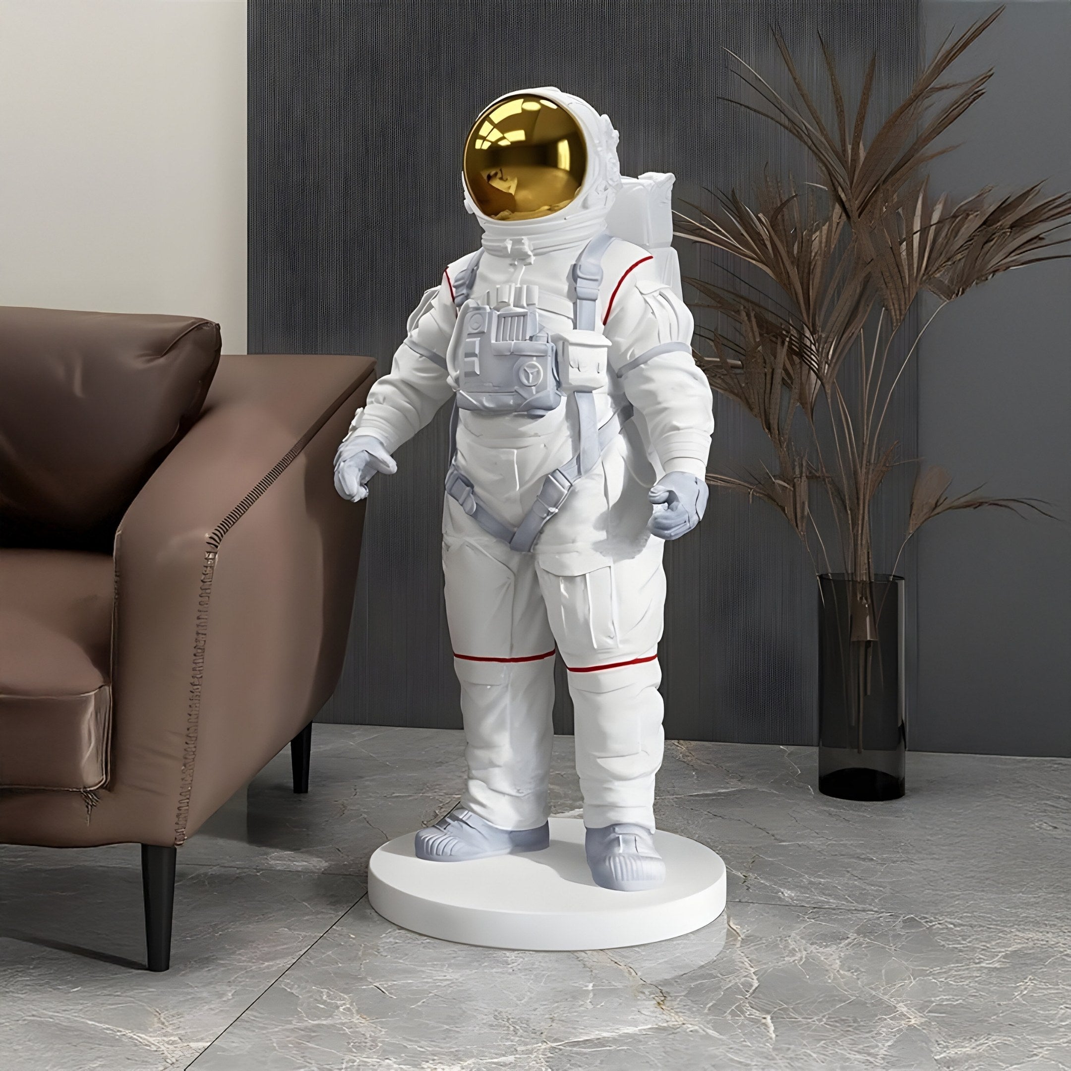 The 88cm White Space Astronaut Standing Sculpture by Giant Sculptures, featuring a golden visor, backpack, and suit lines, elegantly complements a brown couch on marble flooring. It enhances modern decor among tall plants against a dark gray wall.