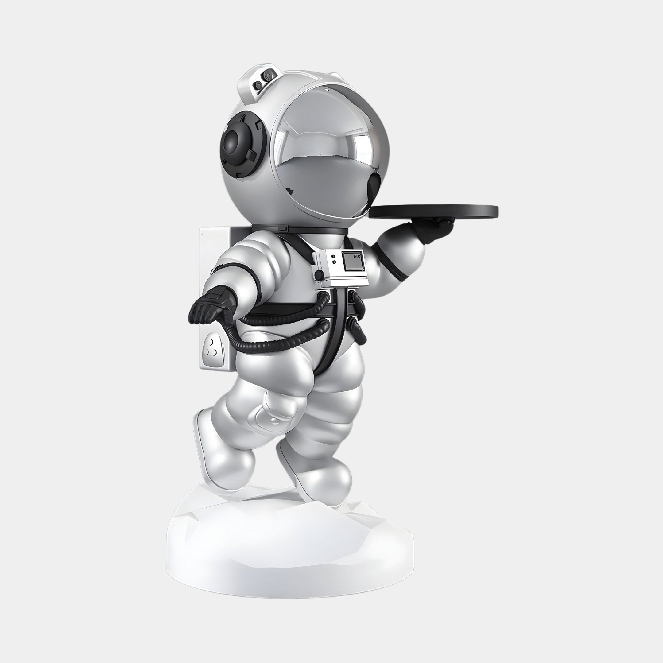 The Astral Silver Astronaut Bear Butler Sculpture by Giant Sculptures features a futuristic astronaut in an Astral Silver suit holding a circular tray, mounted on a white base resembling a wall outlet. Its large, reflective helmet captures cosmic mystery. Height: 90cm.