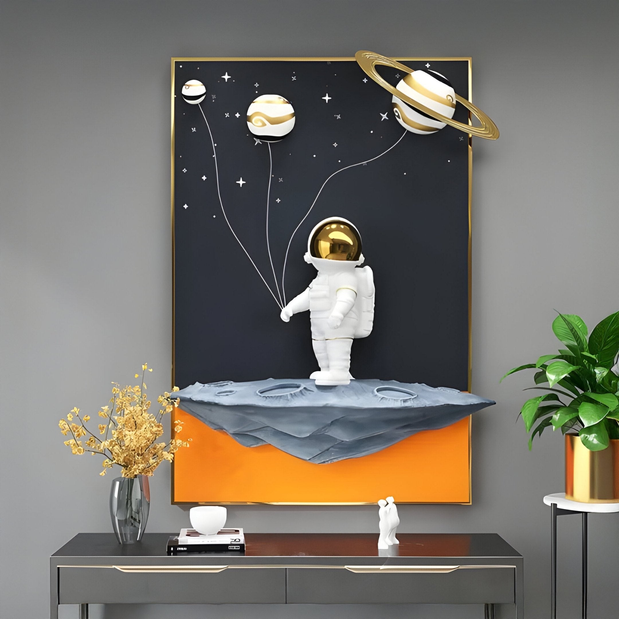 The Giant Sculptures White 3D Stellar Astronaut Planet Balloons Wall Art showcases a cosmic scene with an astronaut and planet-shaped balloons against a starry black background, set on a rock-like platform above decor items and a potted plant.