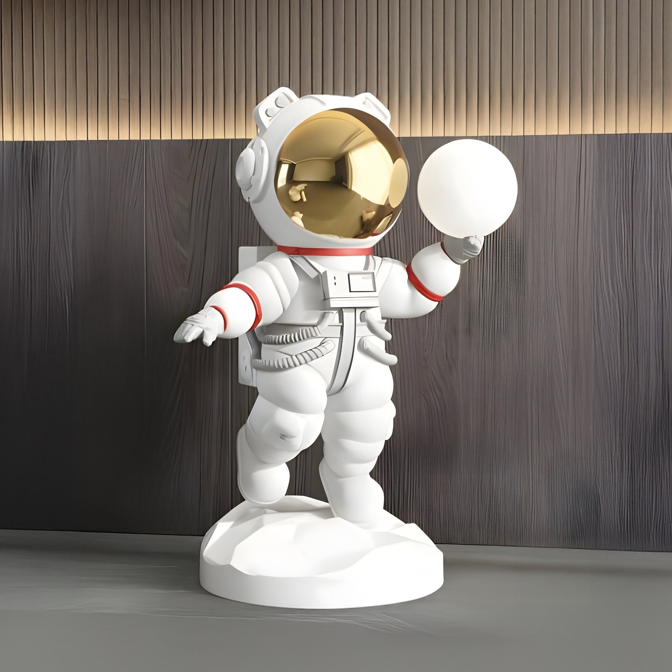 The Nova White Astronaut Bear Glow Sculpture by Giant Sculptures features a 90cm astronaut with a gold visor holding a sphere. The detailed suit, with red accents, stands on a round base against a dark wood background, offering space-themed elements similar to the original design.