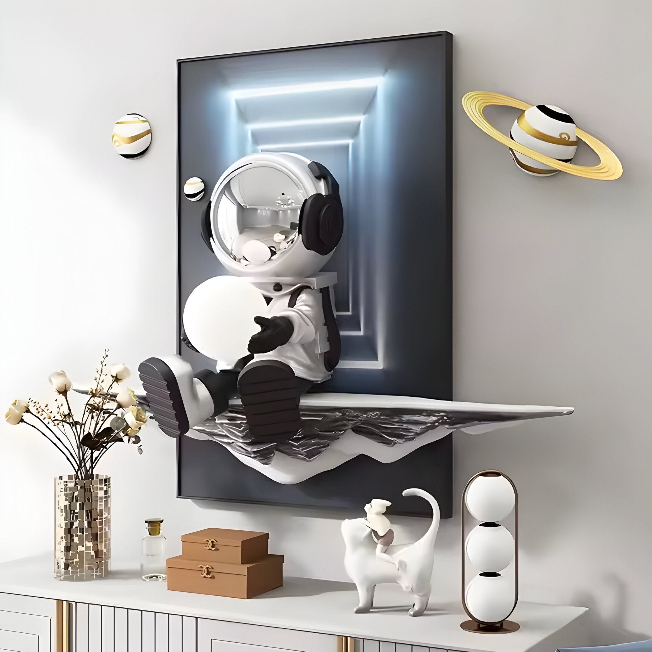 The Silver Astronaut Glow 3D Portal Wall Art by Giant Sculptures features a whimsical silver-lit astronaut with a sphere on a floating metal surface, surrounded by Saturn-like orbs and futuristic décor, including decorative boxes and a cat statue on a cabinet adorned with vases and flowers.