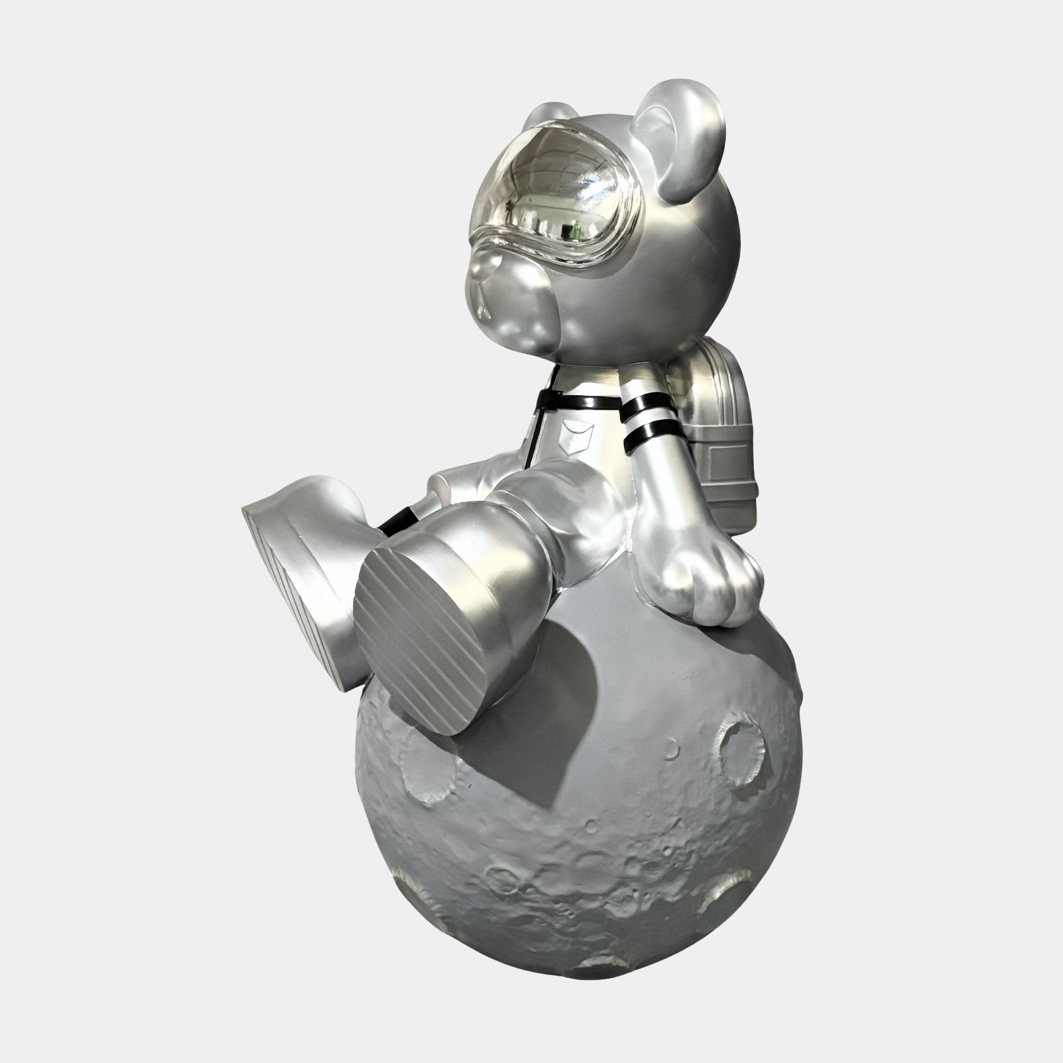 The Giant Sculptures Cosmic Chrome Astronaut Bear Moon Sculpture - 80cm features a shiny astronaut bear with a reflective helmet and backpack, seated on a cratered gray moon against a plain white background.