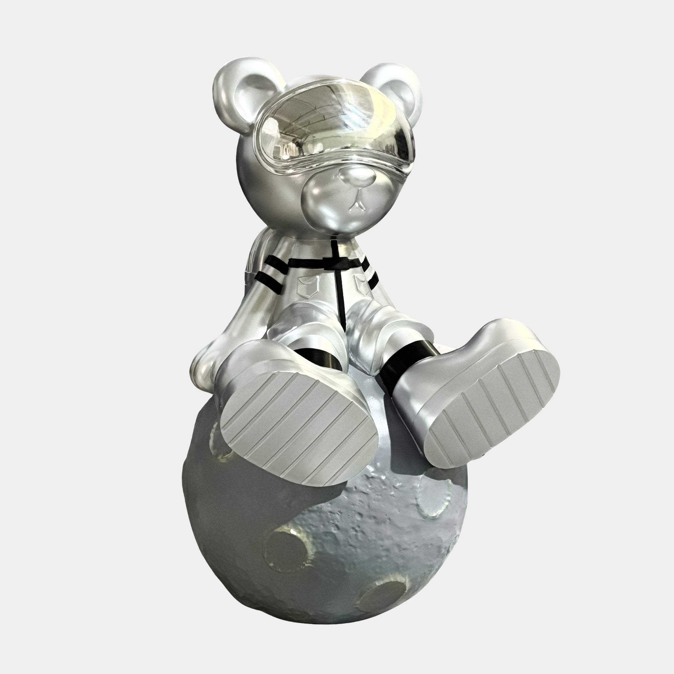 The Giant Sculptures Cosmic Chrome Astronaut Bear Moon Sculpture (80cm) features a shiny silver bear with a reflective visor and spacesuit sitting on a gray, cratered moon against a plain background.