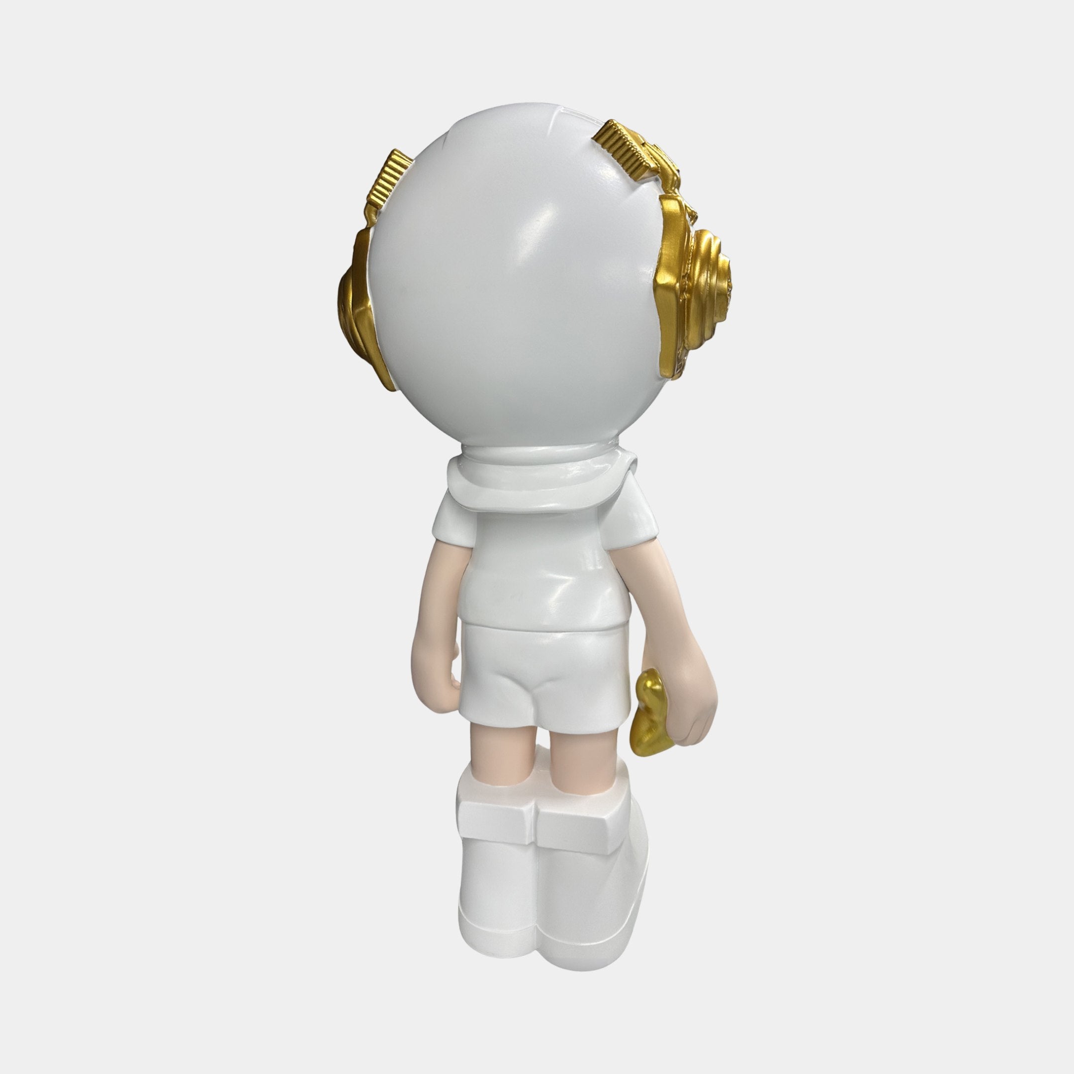 The Cosmic White Astronaut Buddy Sculpture (70cm) by Giant Sculptures features a round-headed figure with gold headphones, short white attire, and a small gold object. Its minimalist design is ideal for futuristic home décor. White background.