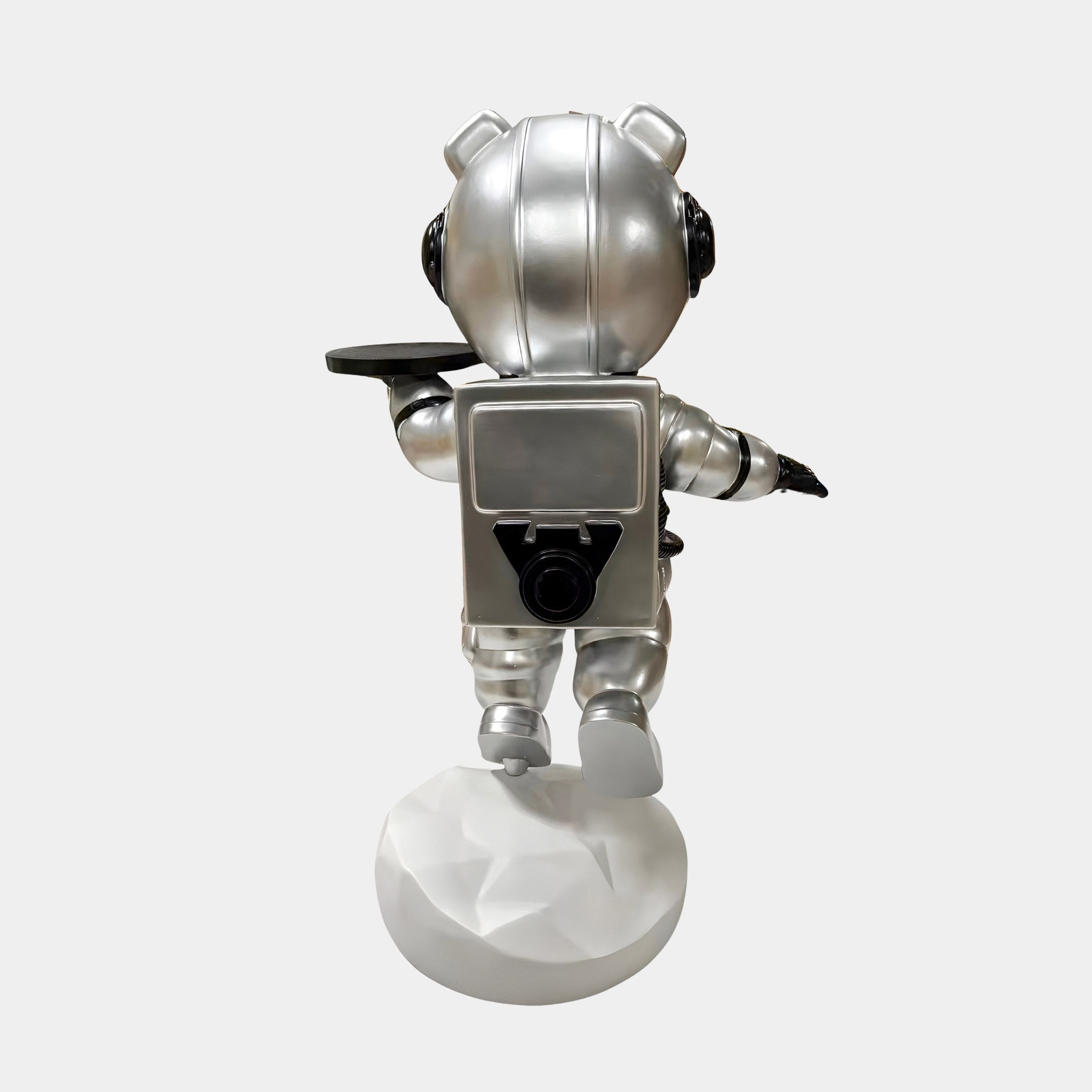 The Giant Sculptures Astral Silver Astronaut Bear Butler Sculpture (90cm) features a silver astronaut bear with a rounded helmet, backpack, and raised arm holding a tray on a white textured base—perfect for space-themed decor.
