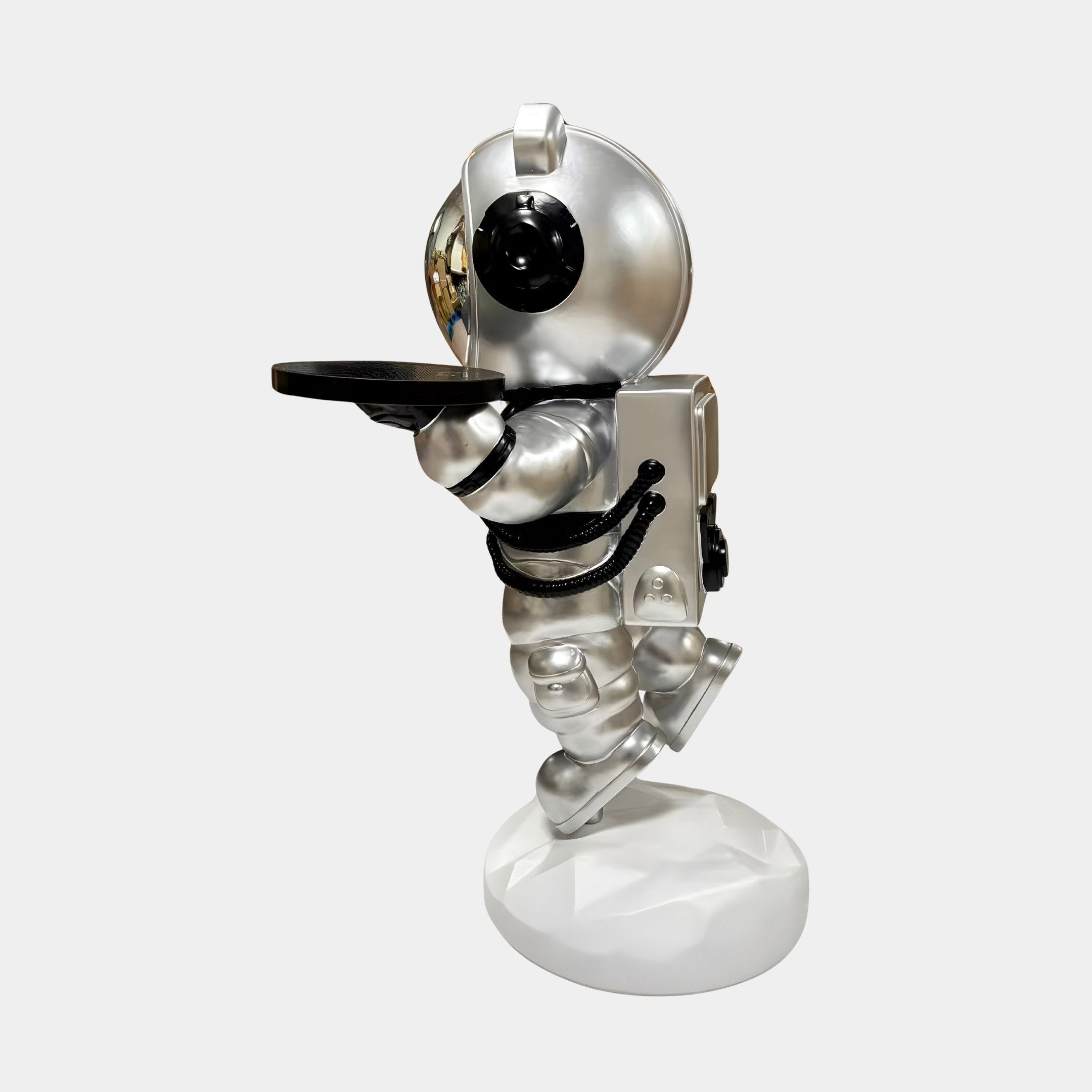 The Astral Silver Astronaut Bear Butler Sculpture (90cm) by Giant Sculptures is a space-themed accent featuring a silver bear astronaut on a white base, holding a black tray with black suit accents and a reflective visor.